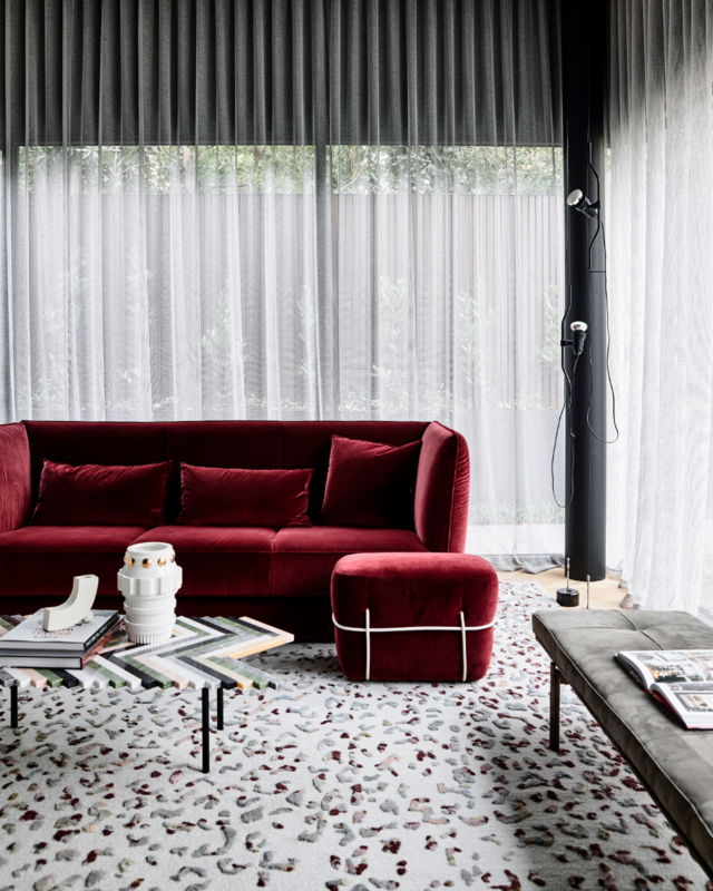 A picture containing a red couch, coffee table and white long curtains. 