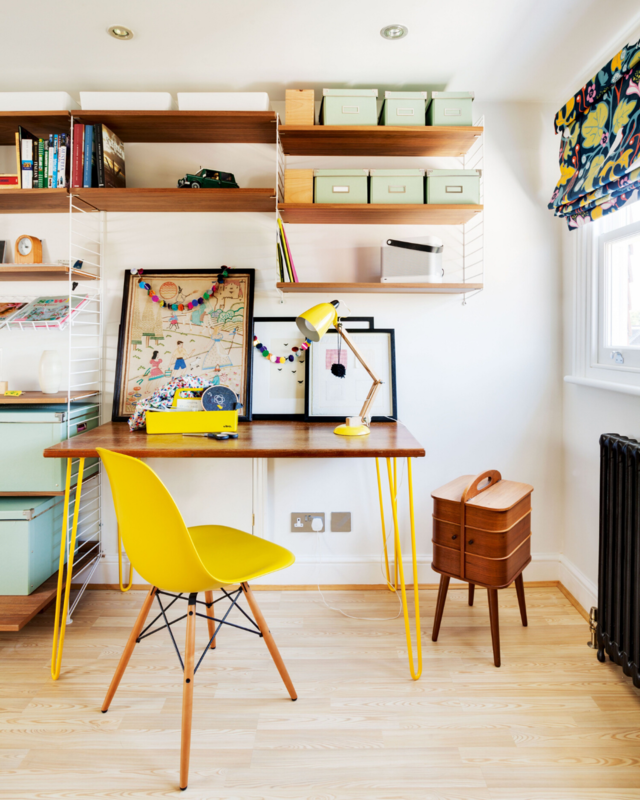 A office in a house with yellow chair and wood desk, several shelves with accessories/decoration. 