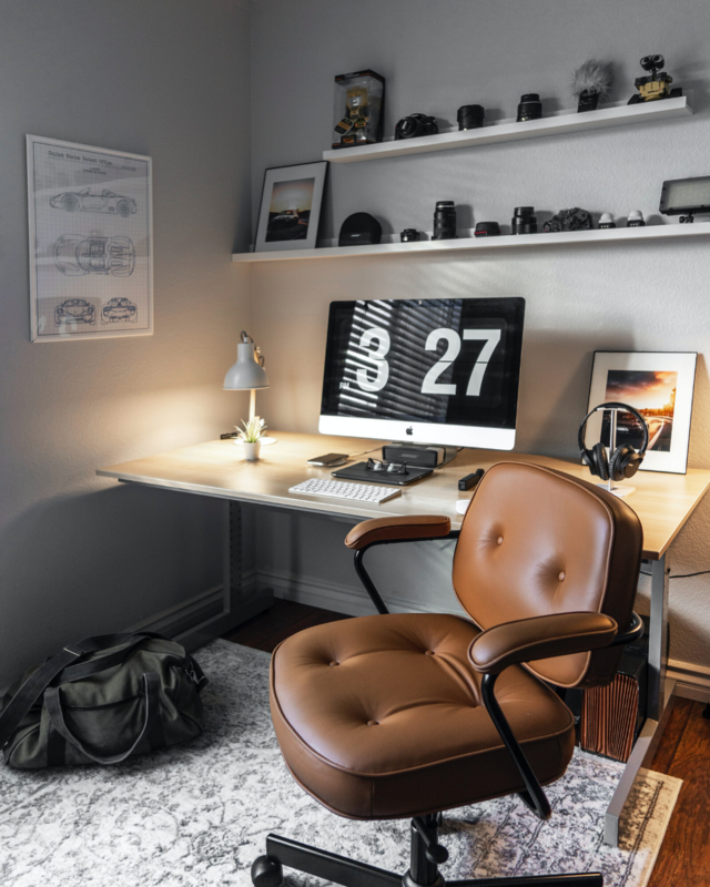 An office room with a desk, leather chair, desktop and several decoration, and a rug under the desk. 